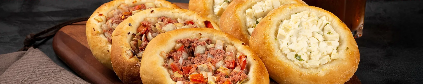 Esfihas abertas de carne e de queijo sobre tábua de madeira.