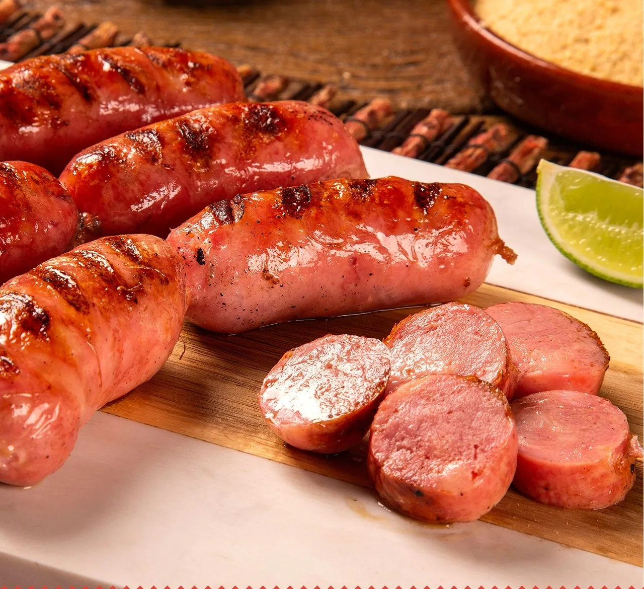 Linguiças grelhadas, inteiras e fatiadas, sobre tábua com limão e farofa.