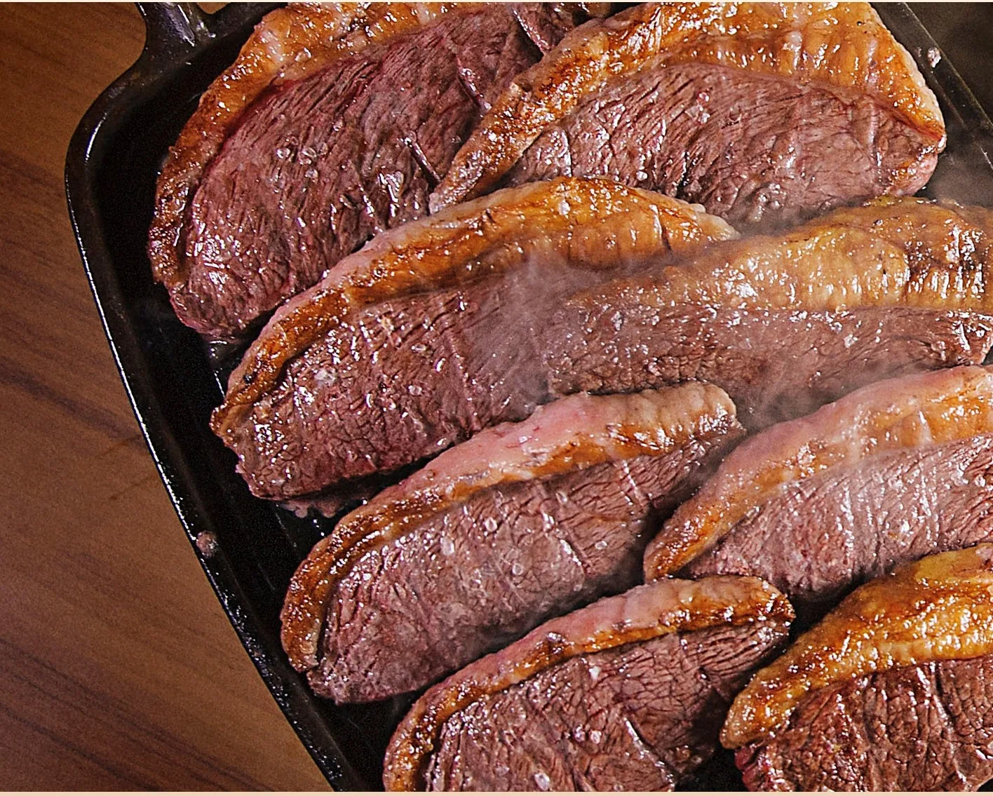 Picanha para duas pessoas fatiada sobre chapa de ferro, em mesa de madeira.