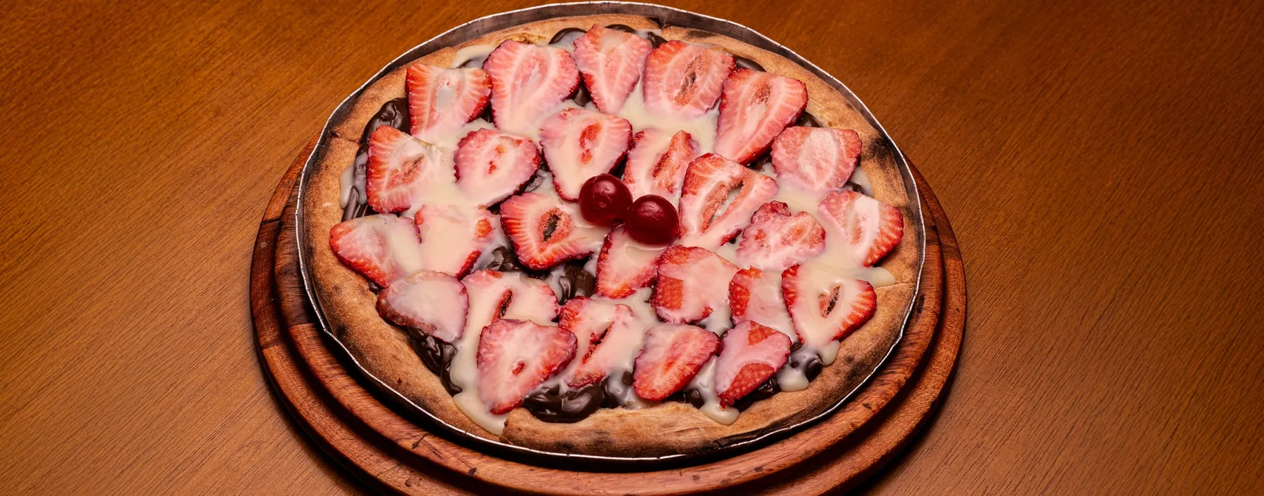Pizza doce de morango com chocolate e leite condensado sobre tábua de madeira.