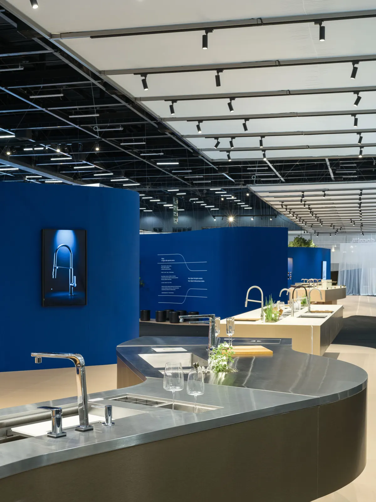 Ilha de cozinha curva em inox com metais Docol, tela emoldurada na parede azul e o texto “Aqui, a água não apenas passa” com linhas fluidas.