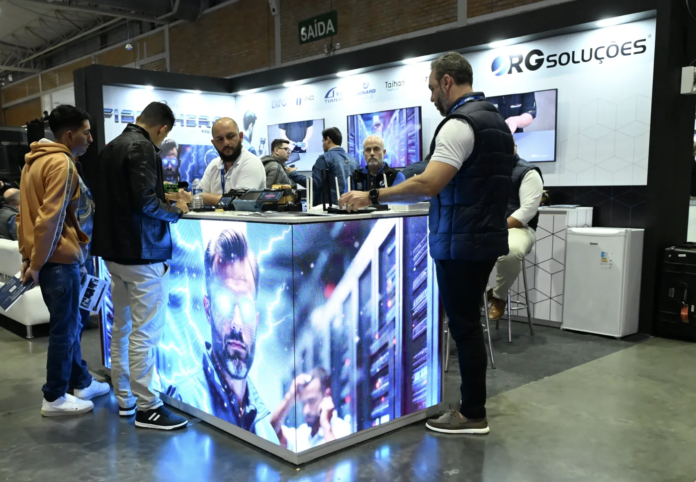 Visitantes no balcão de LED do estande da RG Soluções, com a campanha Fiber Hero em movimento.
