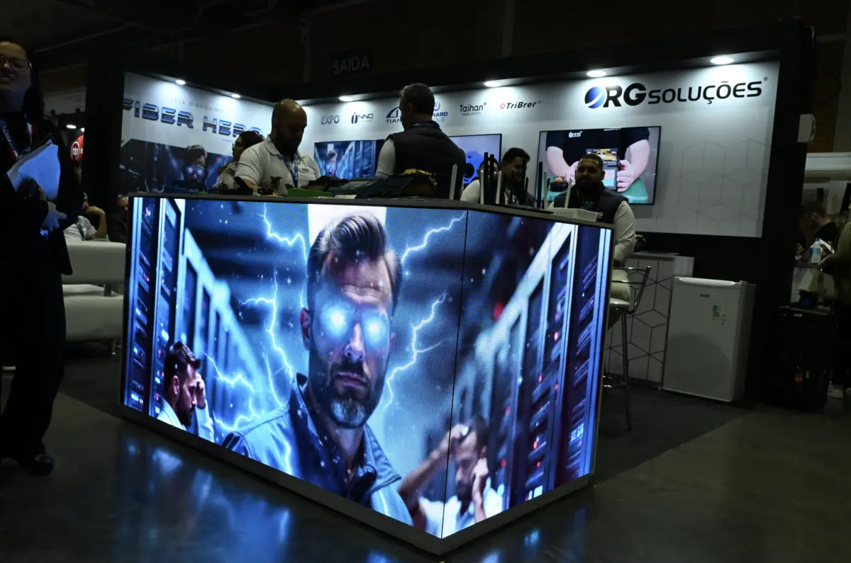Balcão de LED no estande da RG Soluções exibindo o Fiber Hero, com a equipe atendendo ao fundo.