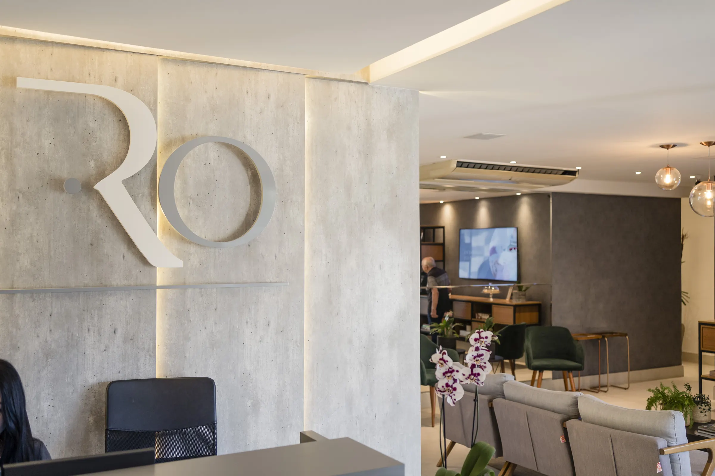 Recepção da Clínica Ricardo Oliveira, com o logotipo RO em relevo na parede de concreto.
