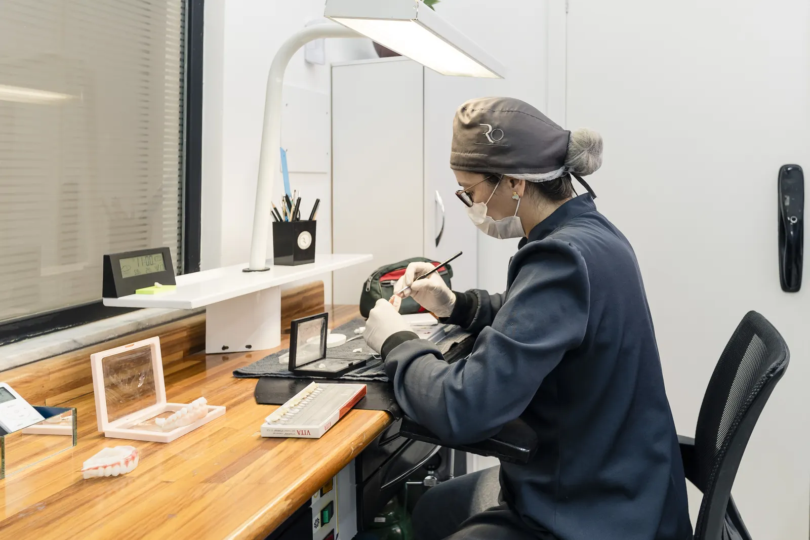 Profissional do laboratório trabalhando em uma peça, em bancada de madeira.