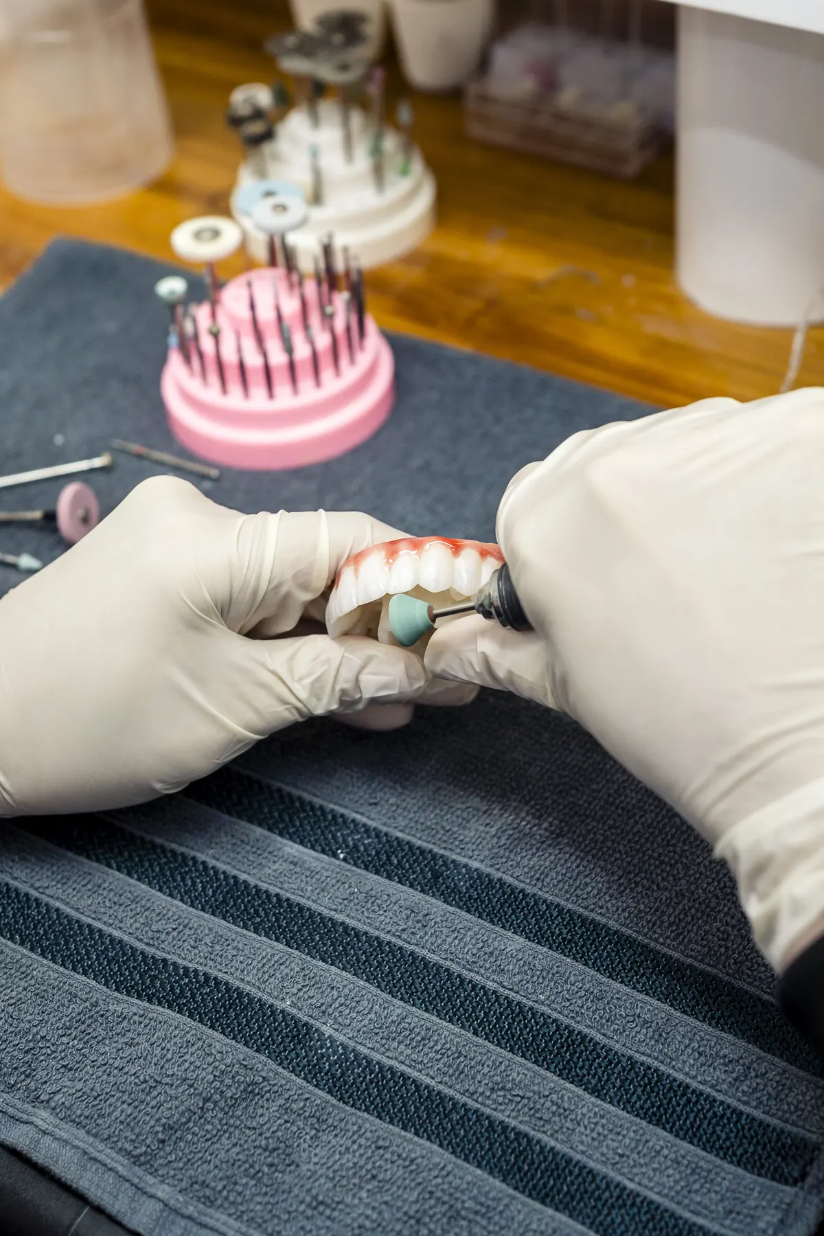 Detalhe de mãos com luvas segurando uma prótese dentária.