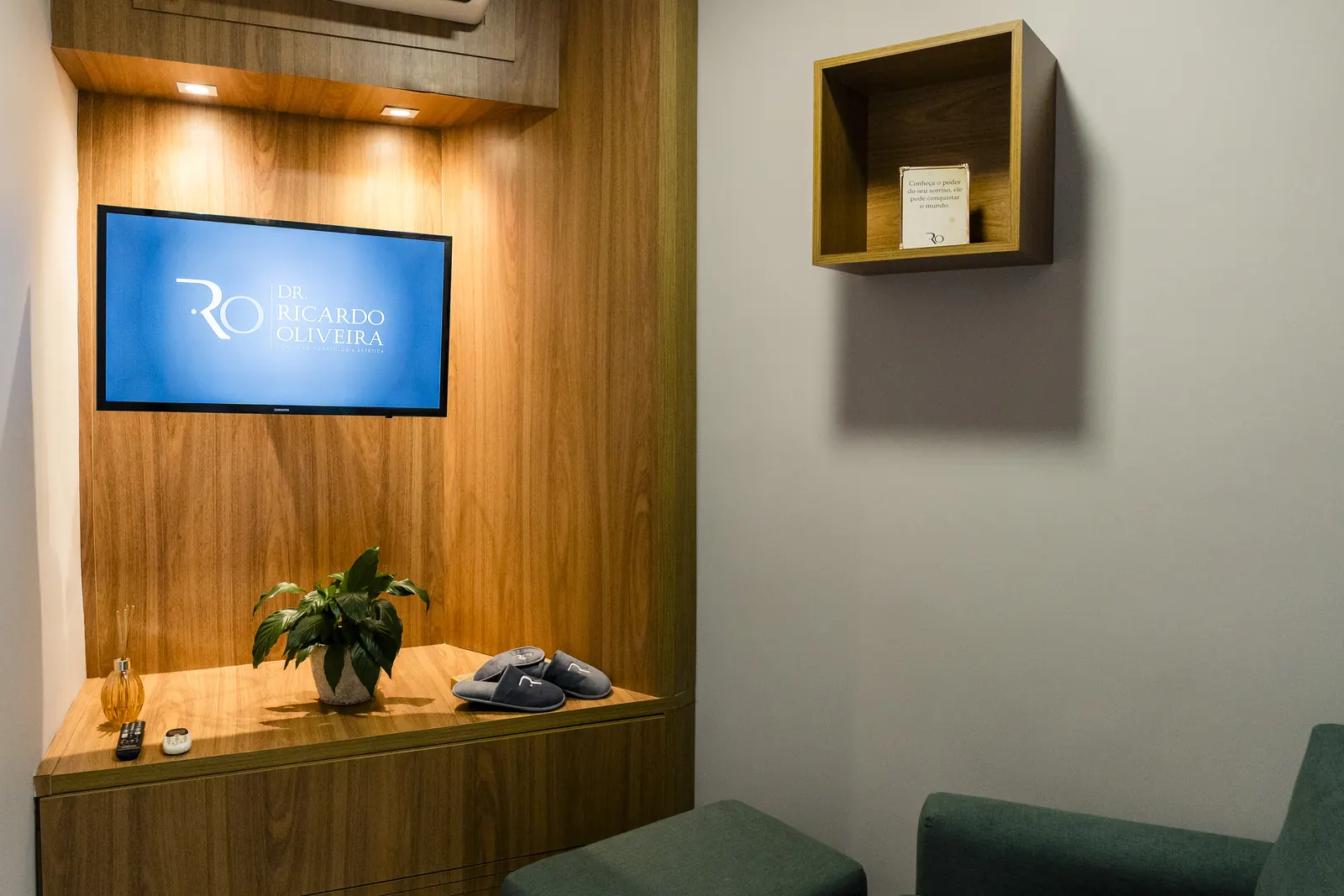 Sala de espera com painel de madeira e televisão com o logotipo da clínica.