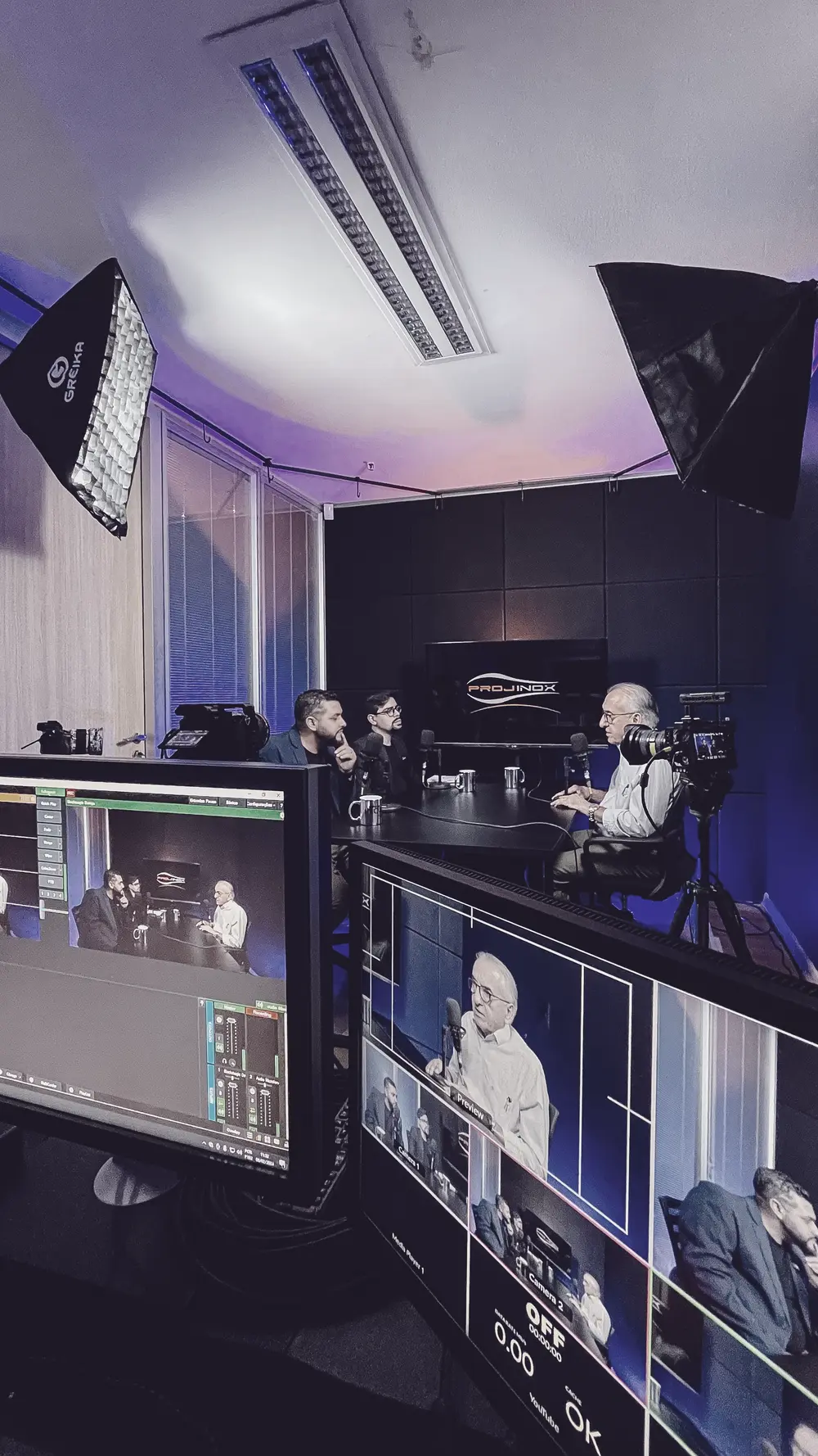 Transmissão ao vivo no estúdio da Buzz 360: monitores da mesa de corte em primeiro plano e o set iluminado ao fundo.